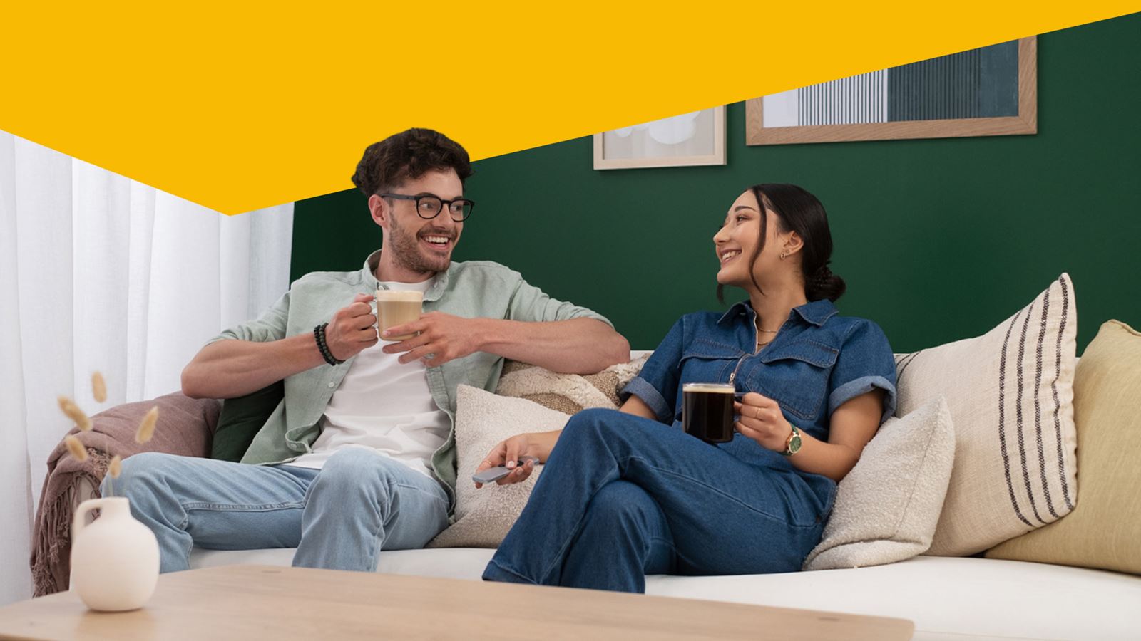 Man and woman drinking coffee on a sofa (with a yellow design element above)