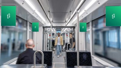 Innenansicht eines öffentlichen Verkehrsmittels mit mehreren Werbeflächen im Wagen; im Hintergrund sind unscharfe Fahrgäste zu sehen.