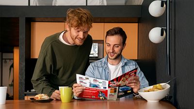 Deux jeunes hommes étudient un catalogue de produits de MediaMarkt à la table du petit-déjeuner.